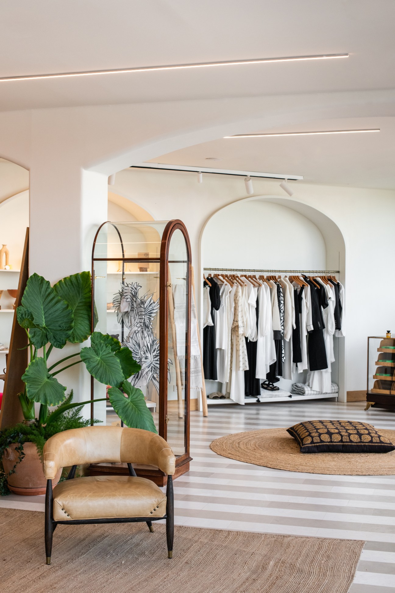 Modern retail interior with white arches, clothing racks, leather chair, and natural lighting