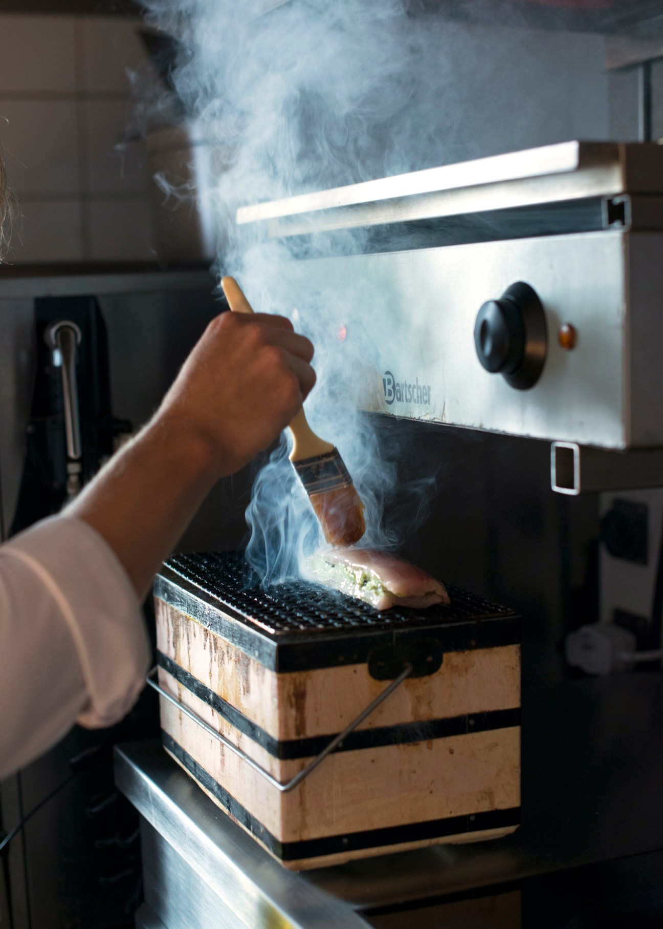 Chef using torch to flame food on grill in professional kitchen with dramatic smoke and fire effects