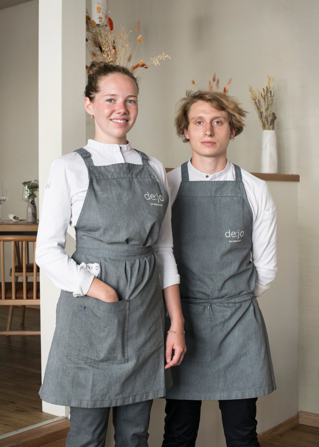 Two chefs in matching gray aprons with 'deja' branding standing together in a modern restaurant interior