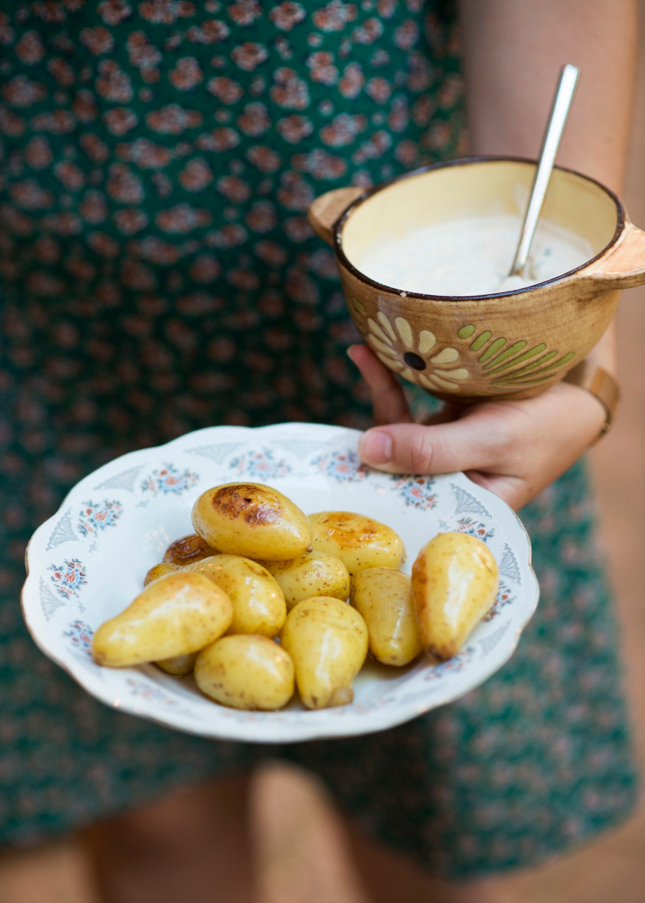Hands holding plate of roasted potatoes and bowl of cream cheese with spoon at L'Un des Sens restaurant