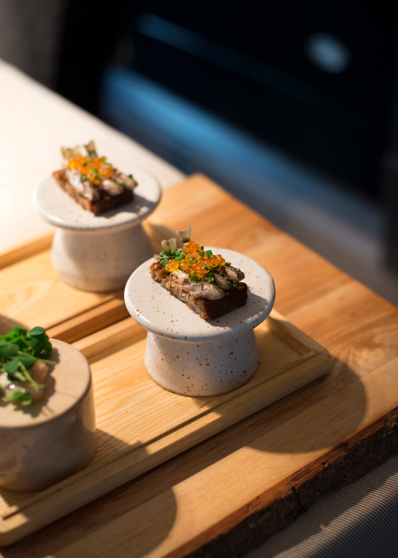 Elegantly plated appetizers with orange garnish served on white speckled ceramic pedestals on wooden board