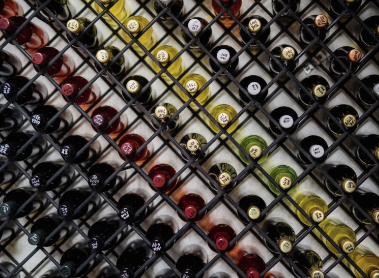 Wine bottles stored in diagonal metal rack showing various labels and bottle colors from white to red