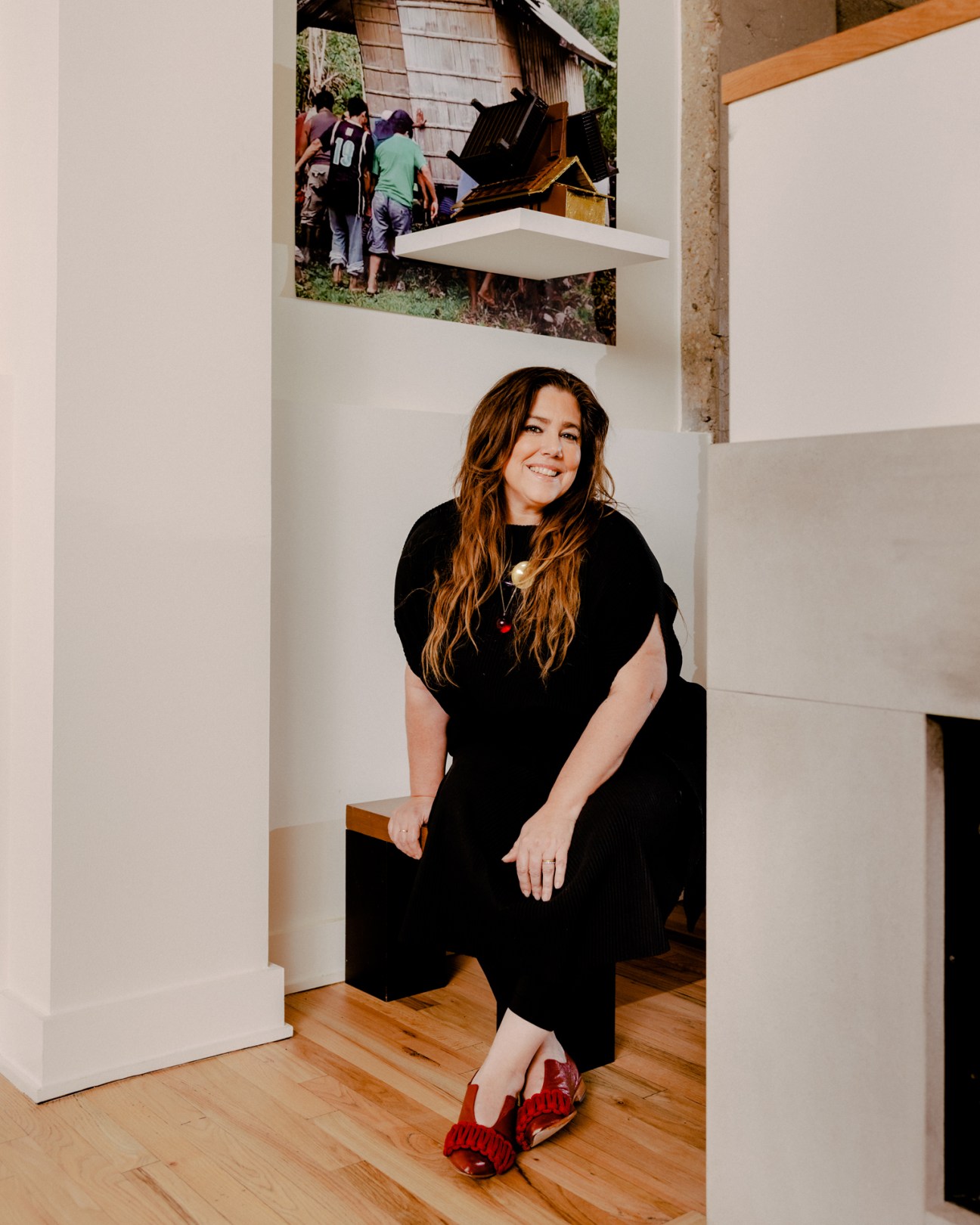 Woman in black clothing seated in a white gallery space with artwork displayed on walls.