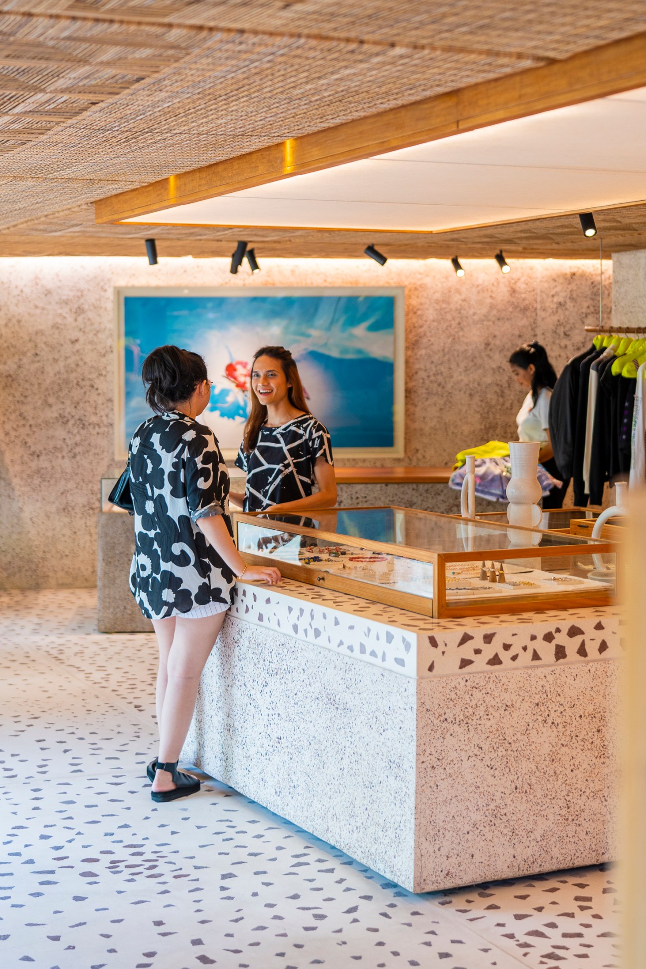 Two women conversing at a modern retail counter with terrazzo surfaces and clothing displays in background