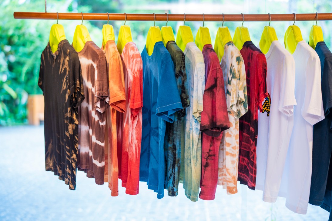 Colorful tie-dye T-shirts hanging on wooden clothing rack with yellow hangers