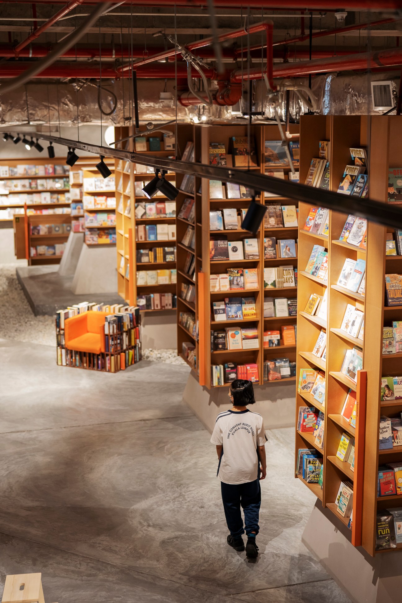Modern bookstore interior with wooden shelving displaying books and a person browsing below exposed ceiling