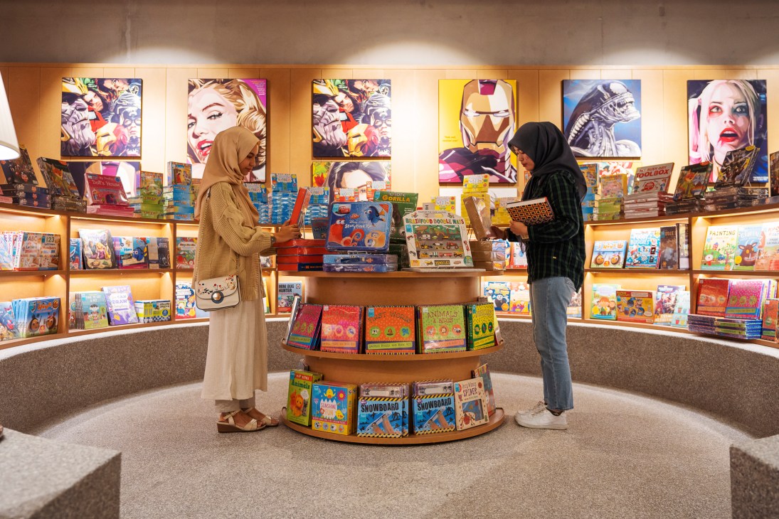 Two women in headscarves browsing books in a modern bookstore with comic book artwork on the walls