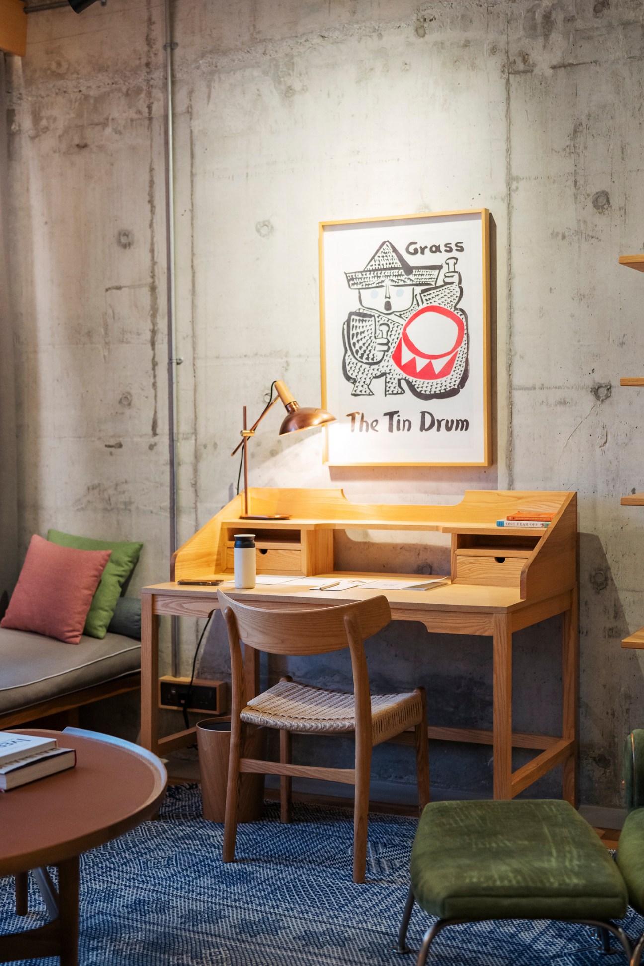 Modern wooden desk with brass task lamp, framed poster reading 'The Tin Drum', chair and green ottoman