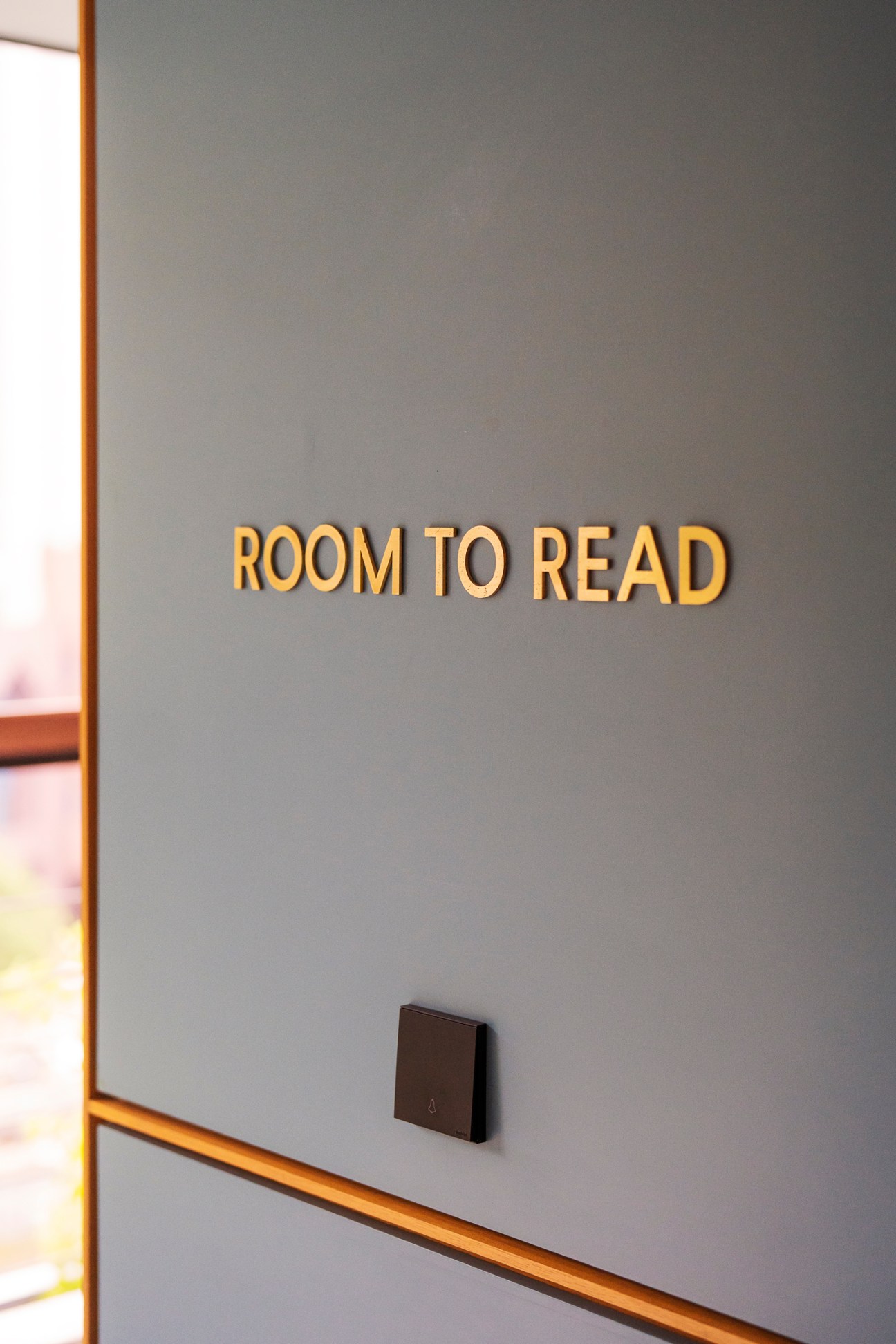 Gold lettering reading 'ROOM TO READ' on a grey wall with a dark switch plate below