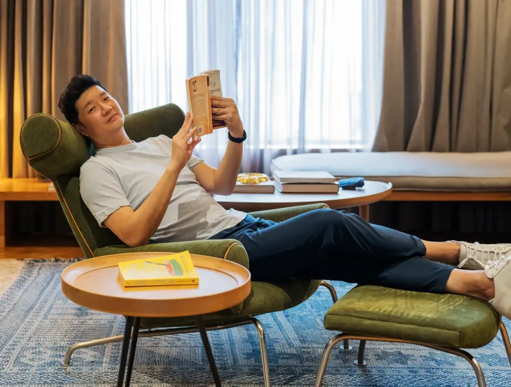 Kloé Hotel founder Ng Ping Ho relaxing in a green chair while reading a book