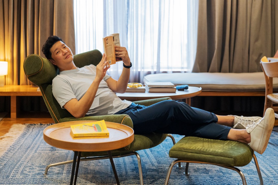 Kloé Hotel founder Ng Ping Ho relaxing in a green chair while reading a book