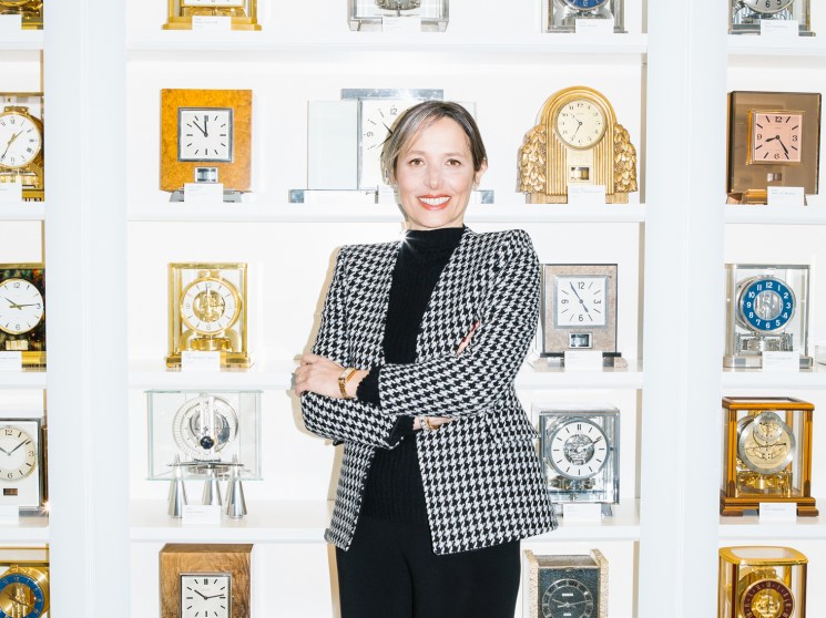 Catherine Rénier, CEO of Jaeger-LeCoultre, standing in front of wall display of luxury clocks and timepieces