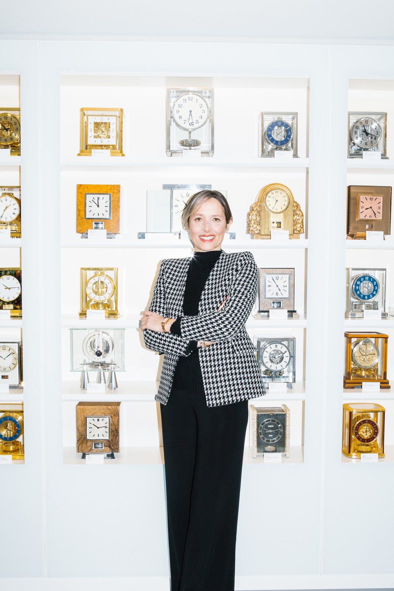 Catherine Rénier, CEO of Jaeger-LeCoultre, standing in front of wall display of luxury clocks and timepieces