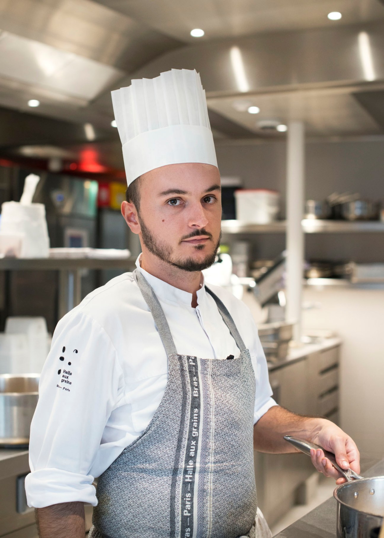 Chef in white uniform and hat working in professional kitchen at La Halle aux Grains restaurant
