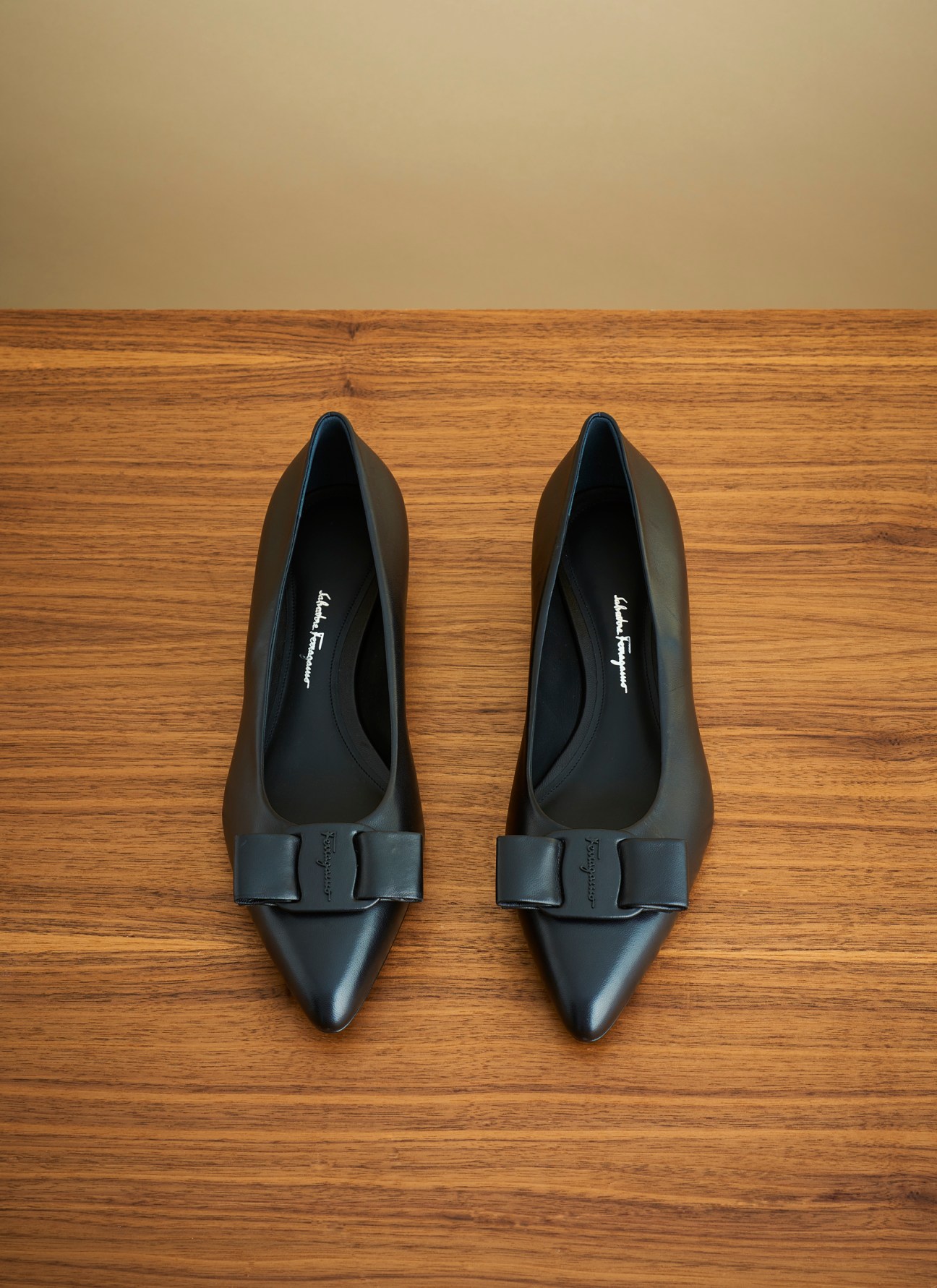 Black pointed-toe ballet flats with bow detail on wooden floor