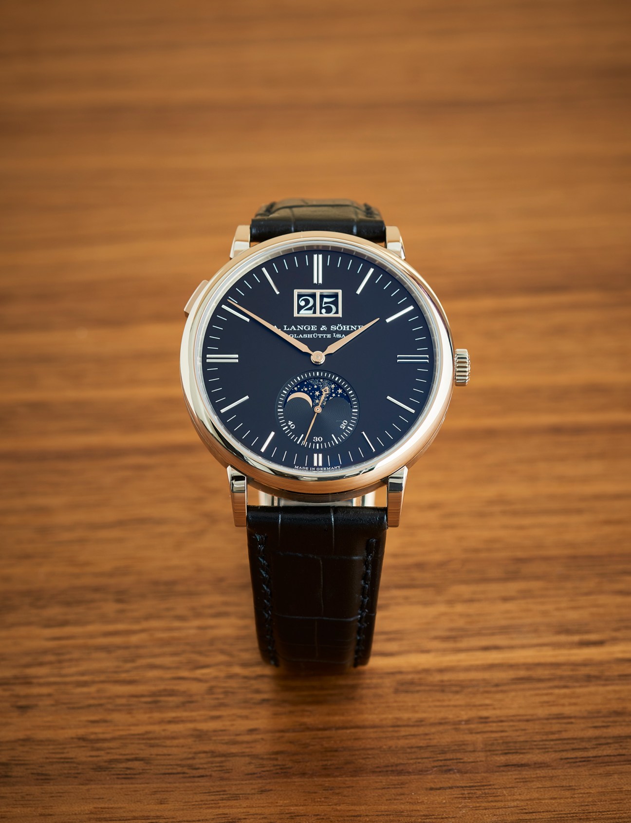 A Lange & Söhne Saxonia Moon Phase watch with blue dial, gold case and black leather strap on wooden surface