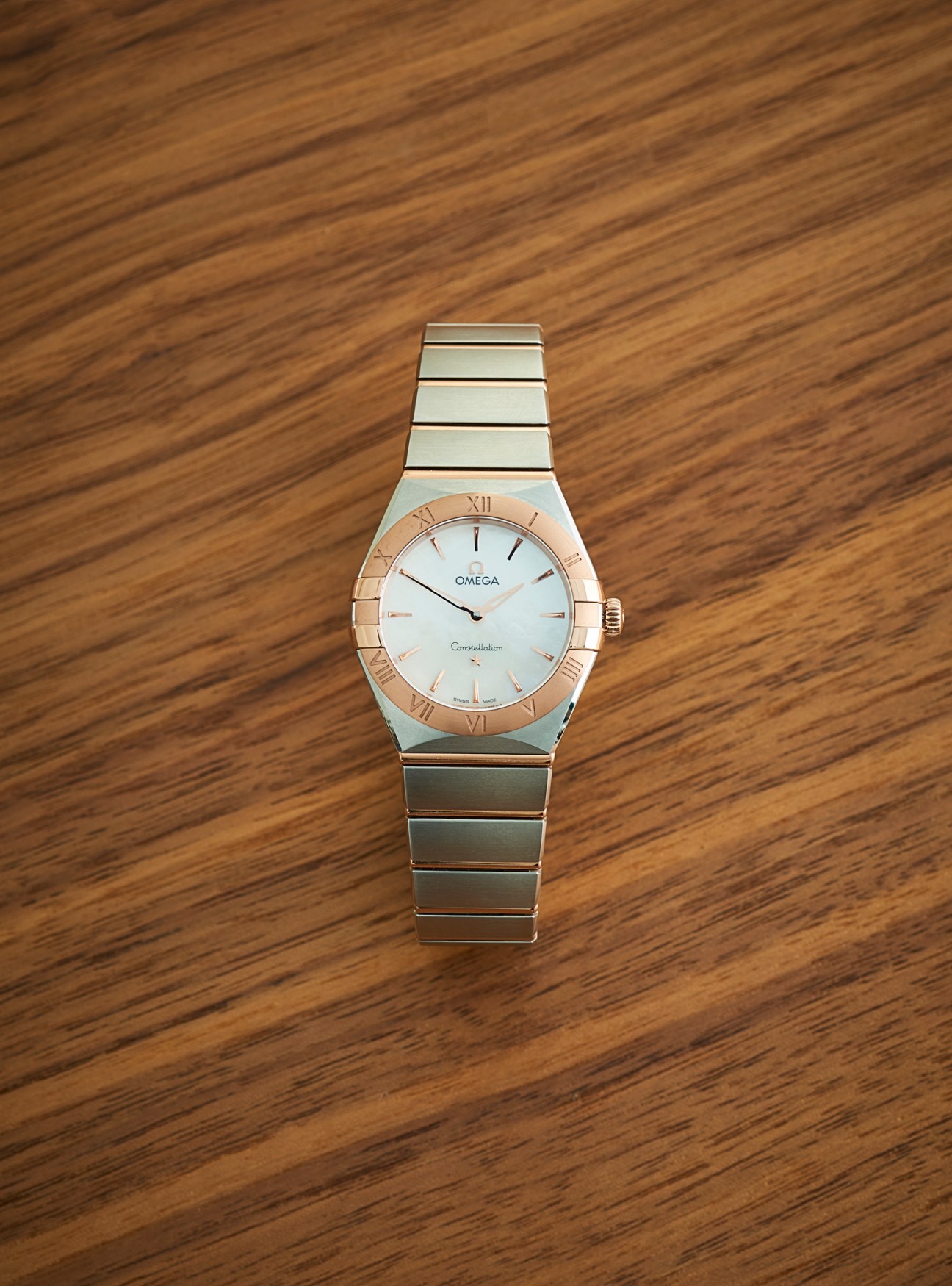 Omega Constellation watch with two-tone metal bracelet and white dial on wooden surface