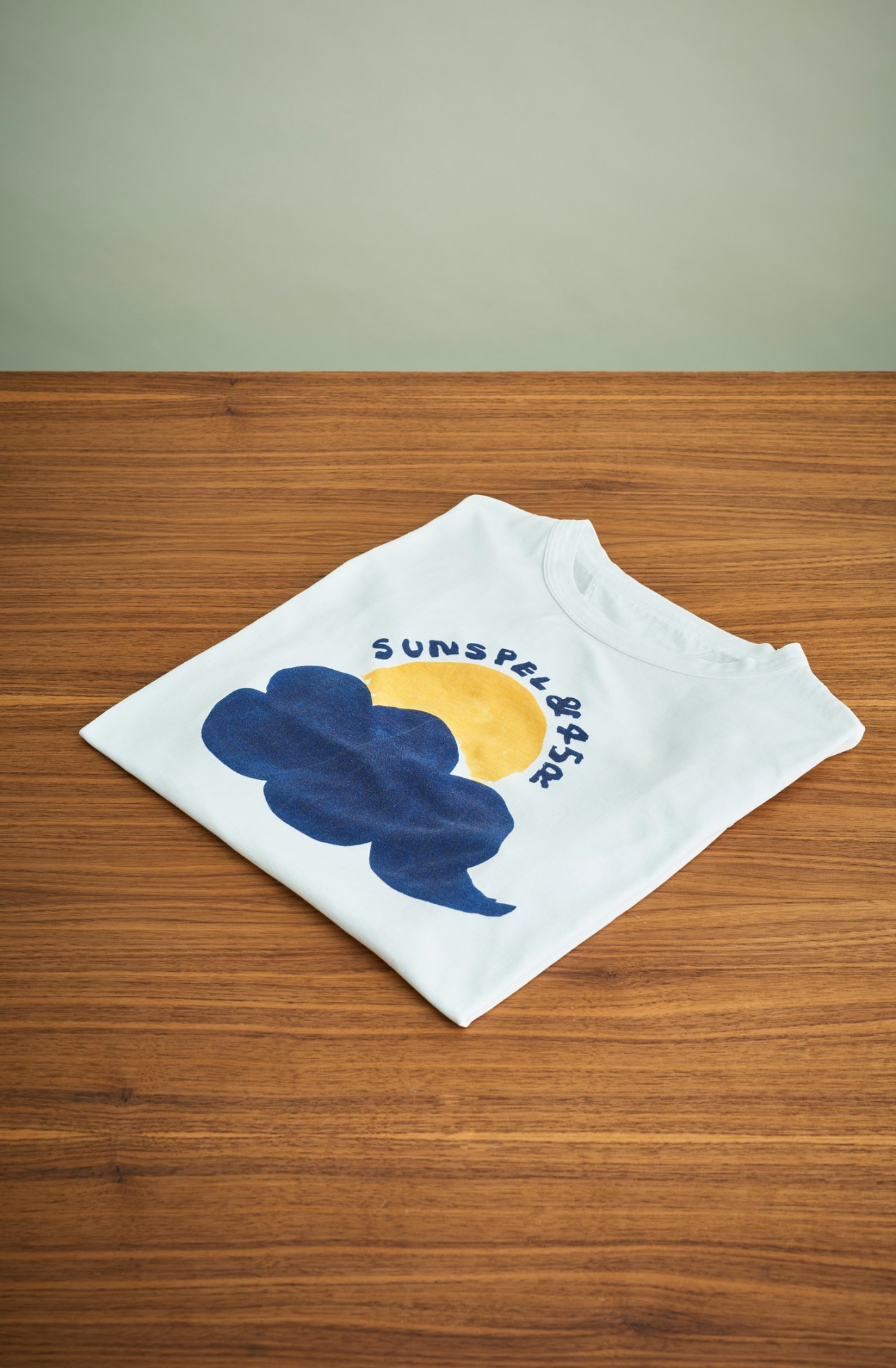 White t-shirt with blue cloud and yellow sun graphic design featuring Sunspel branding