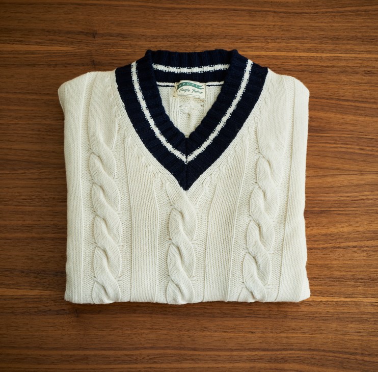 Cream cable-knit sweater with navy and white striped V-neck collar folded on wooden surface