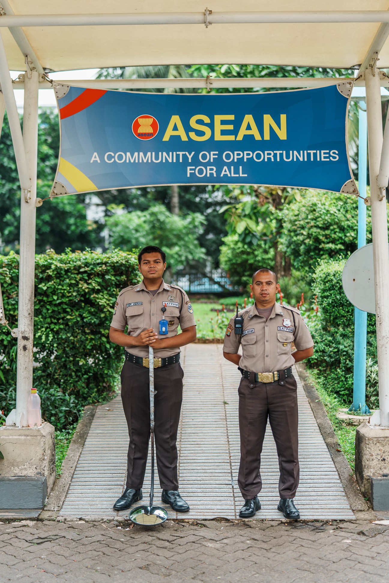 Two security guards in uniform standing under an ASEAN banner on a wooden walkway