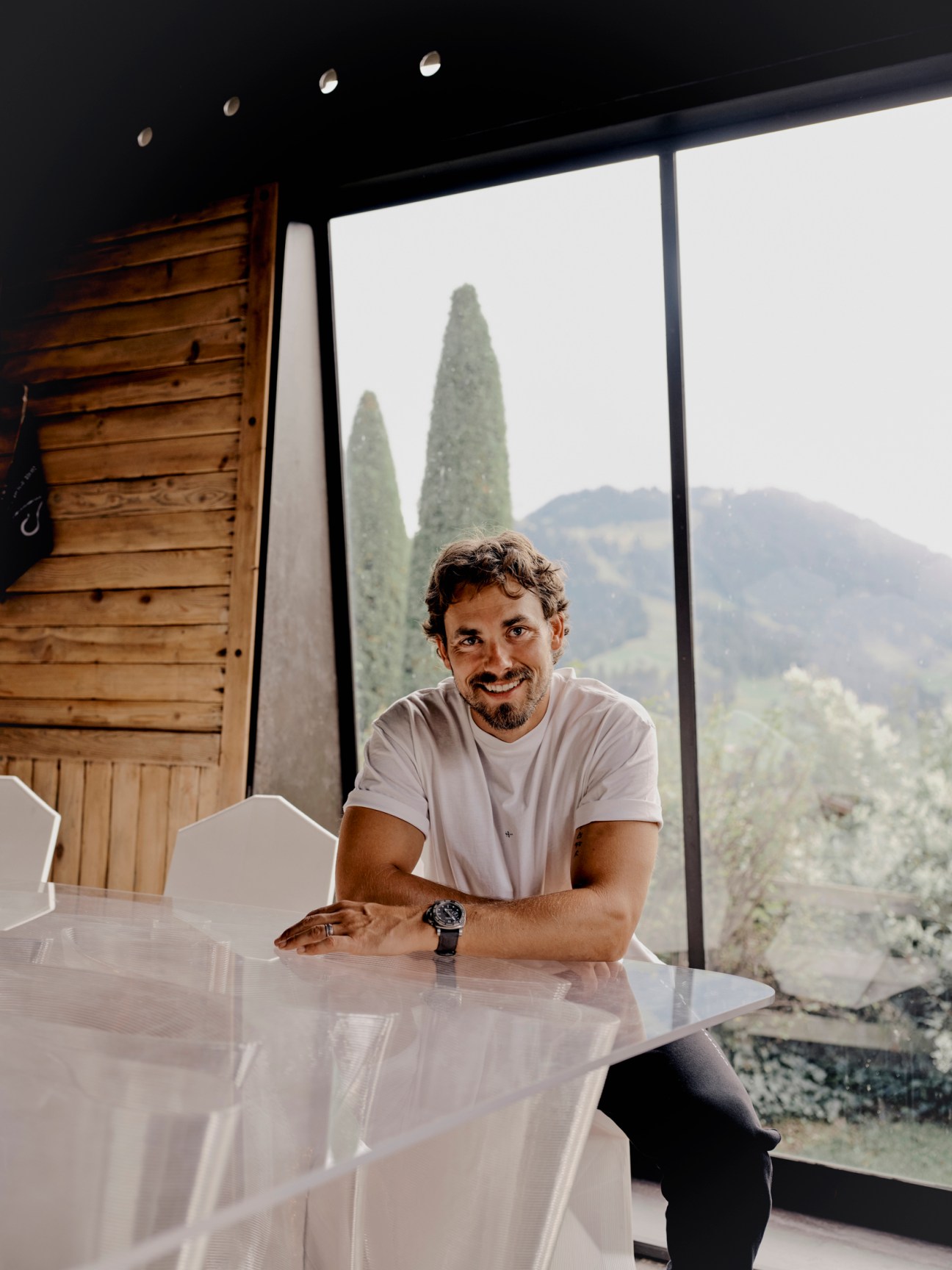 Nachson Mimran sits at a white table in a modern room with floor-to-ceiling windows overlooking cypress trees and rolling hills.