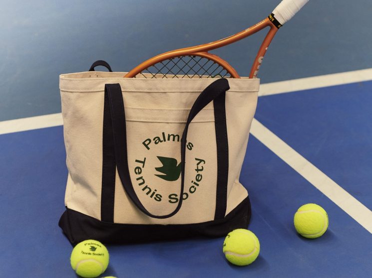 Palmes Tennis Society canvas tote bag with tennis racket and yellow tennis balls on blue court surface