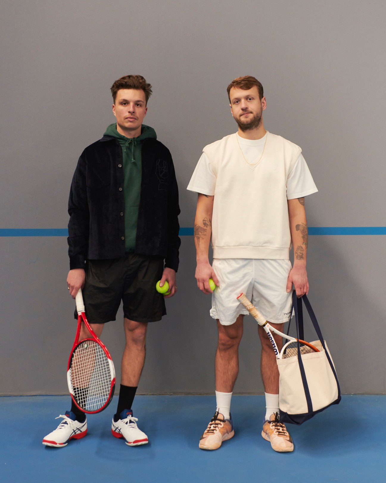 Two men in tennis attire holding rackets and tennis balls on a blue court