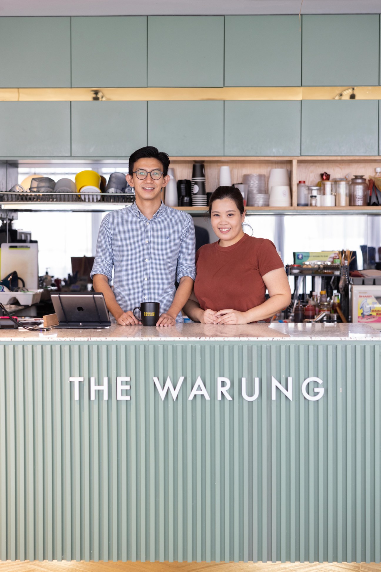 Ooi Zhi Yi and Jocelyn Yew, co-founders of the Warung café, standing behind counter in modern green-toned café