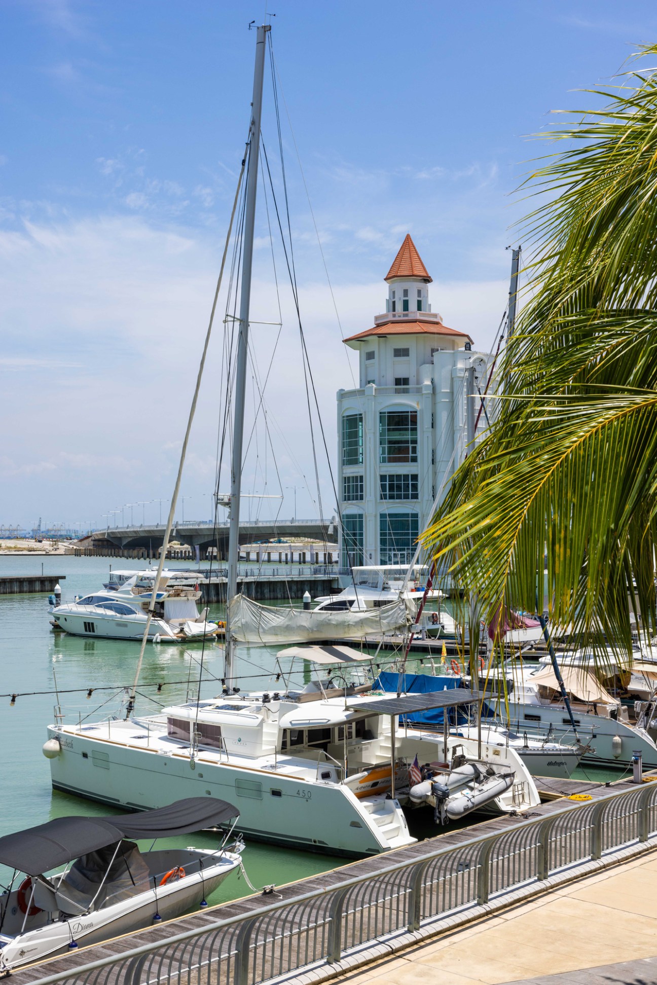 Marina with white boats and catamarans moored at docks, distinctive white tower with red roof in background