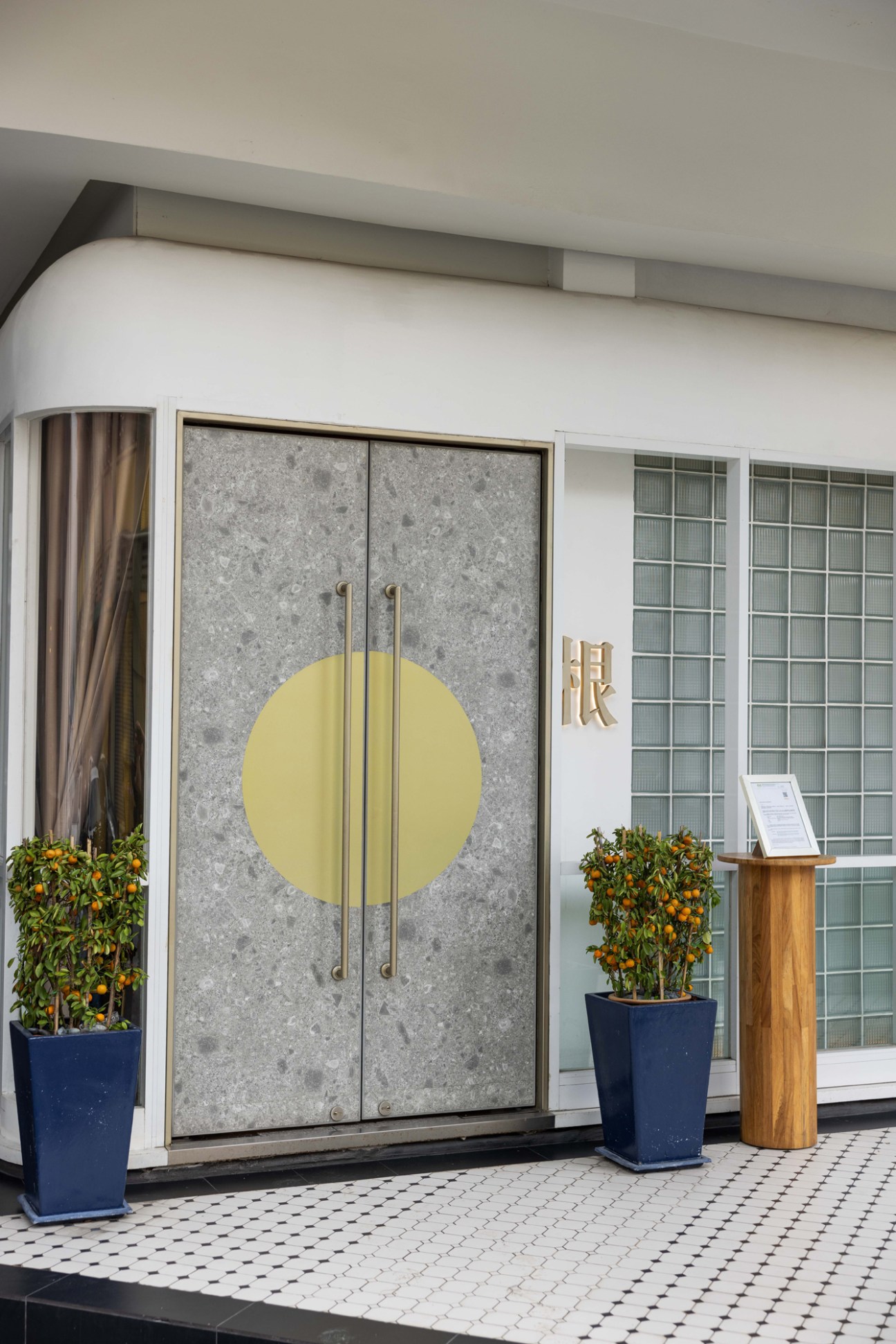 Modern restaurant entrance with concrete doors featuring yellow circle design and brass handles