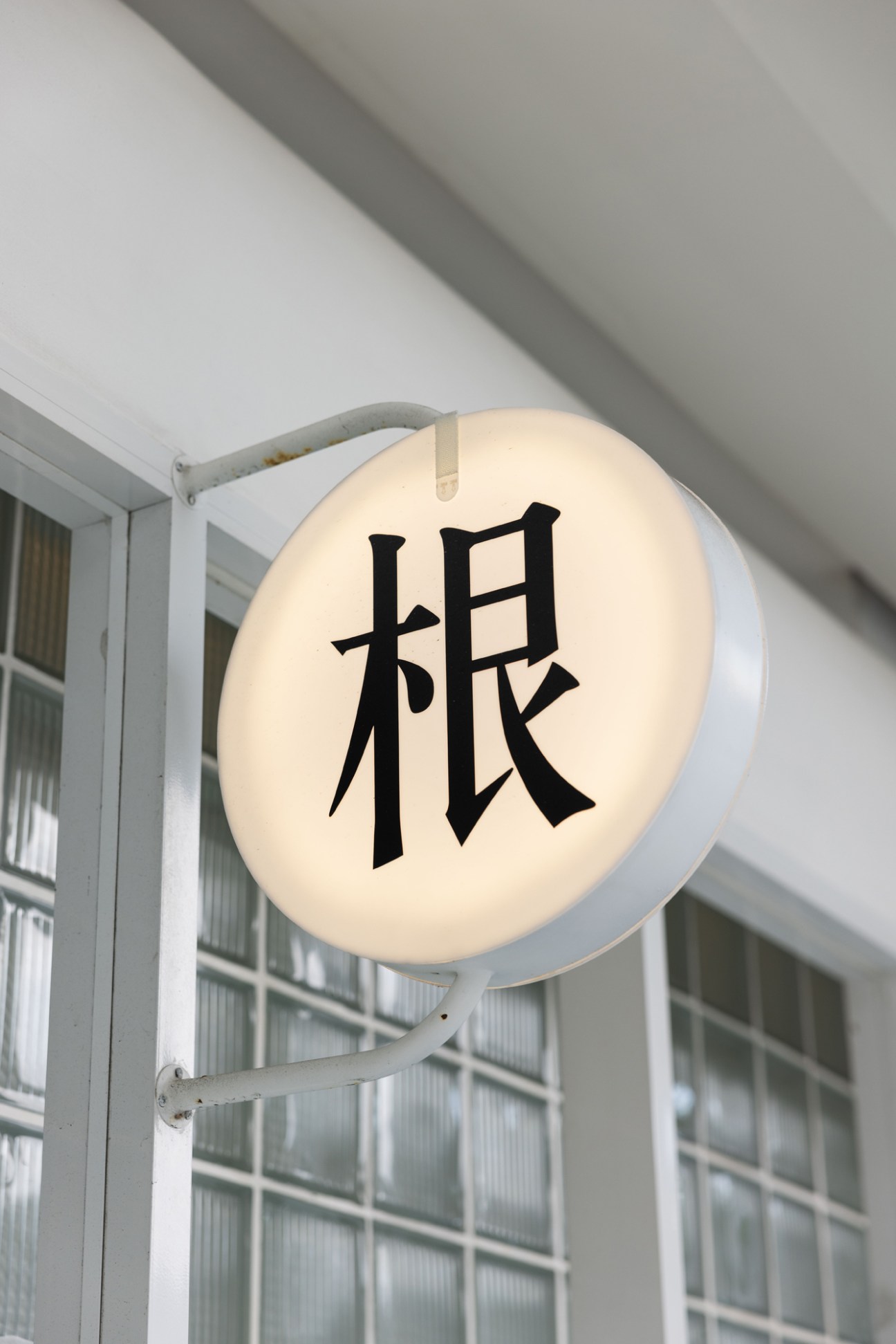 Illuminated circular sign with Chinese character mounted on white metal bracket outside building