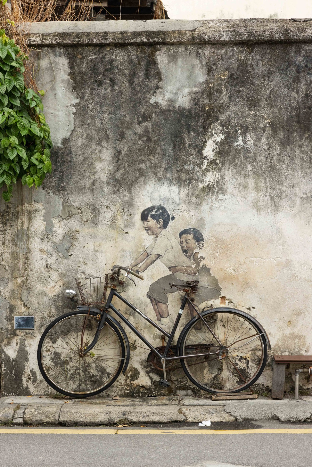Street art mural by Ernest Zacharevic showing two children on a bicycle painted on weathered wall