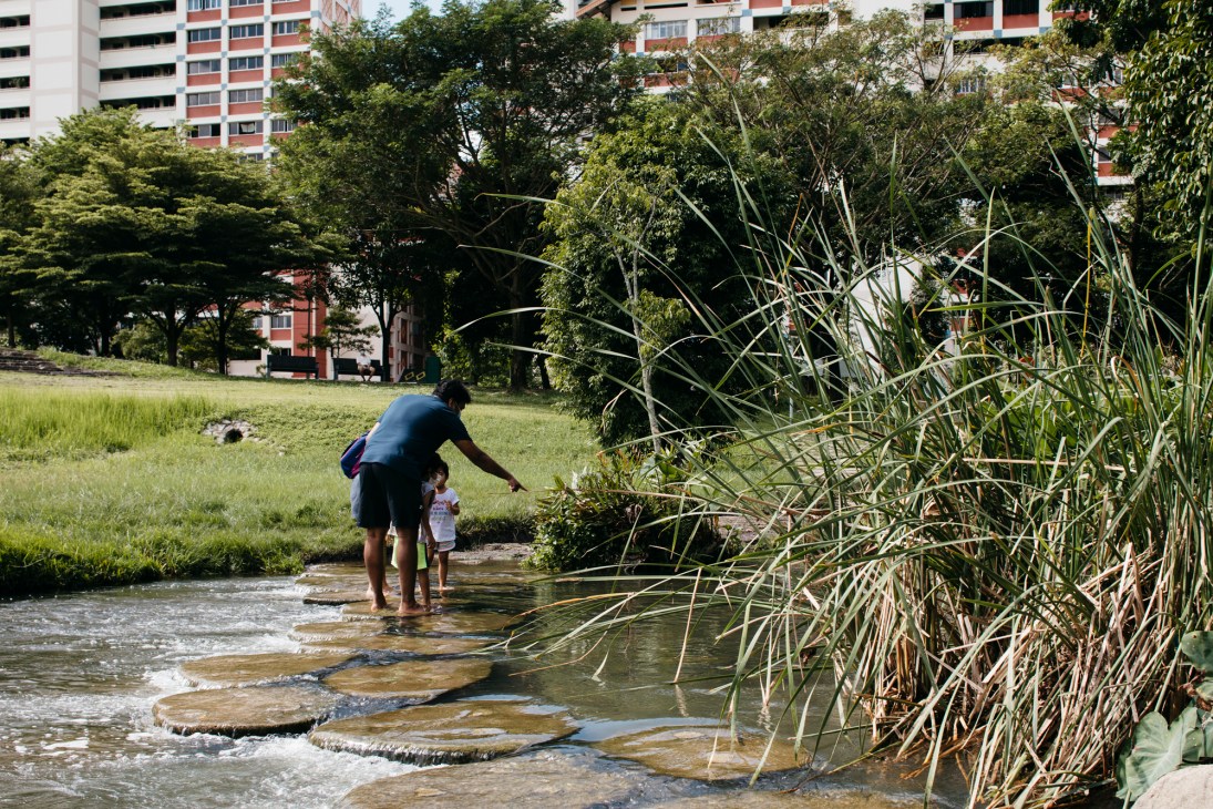 Adult and child crossing river on circular stepping stones in Singapore park