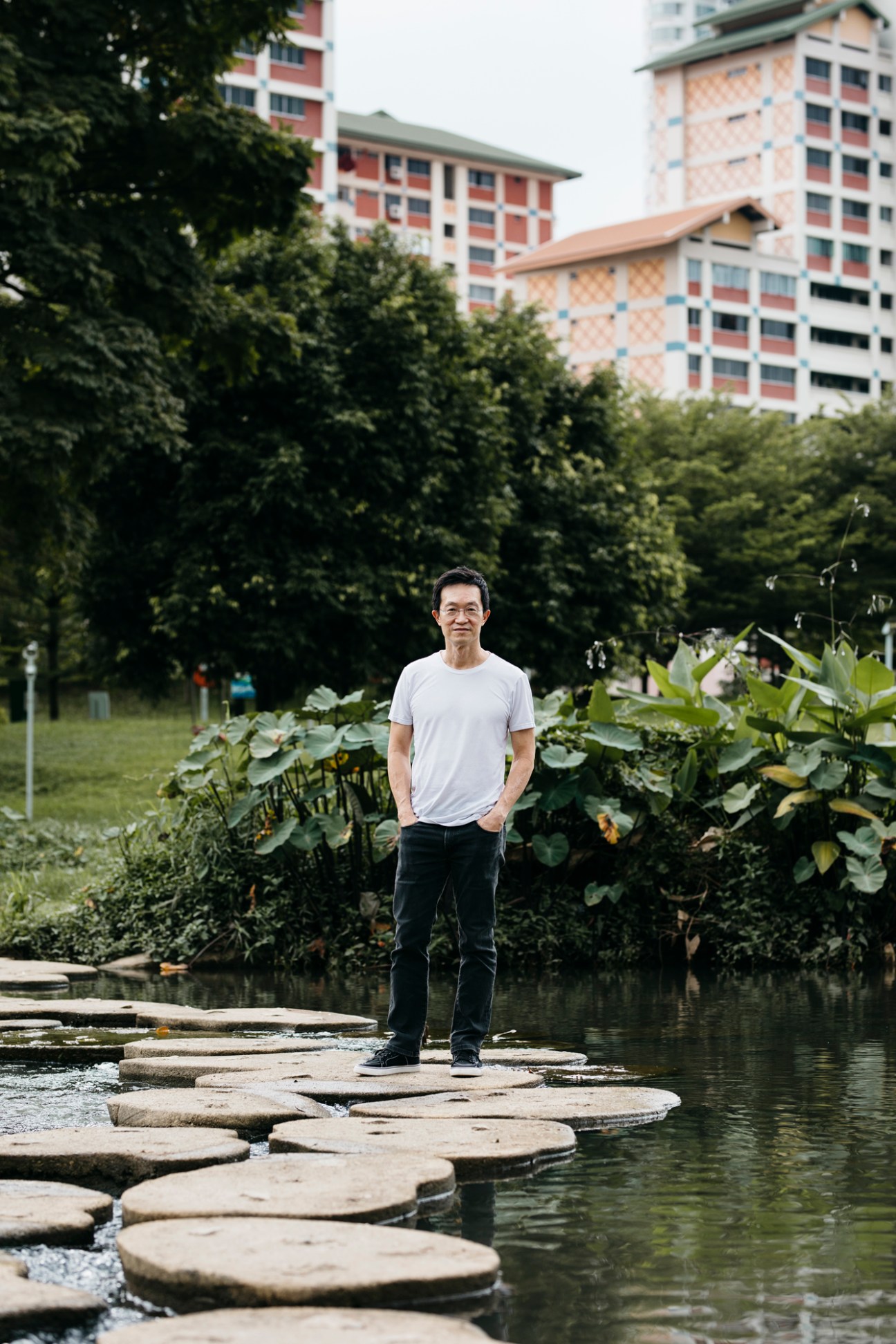 Leonard Ng standing on circular stepping stones in water with lush vegetation and apartment buildings in background