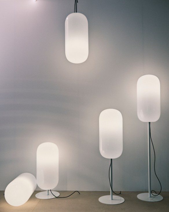 Multiple white oval-shaped pendant and floor lamps displayed against a gray wall