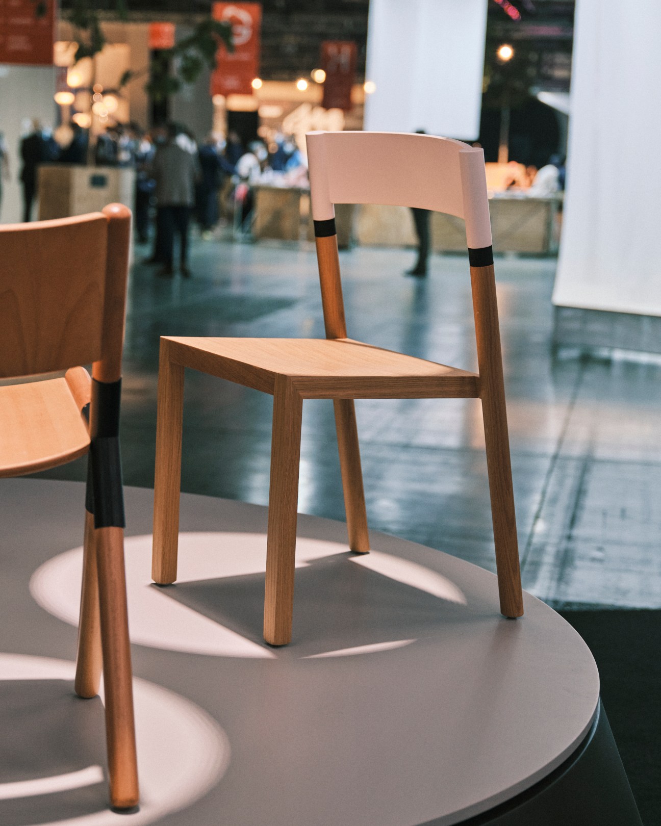 Modern wooden chairs with curved backs and black accent bands displayed on white circular platforms