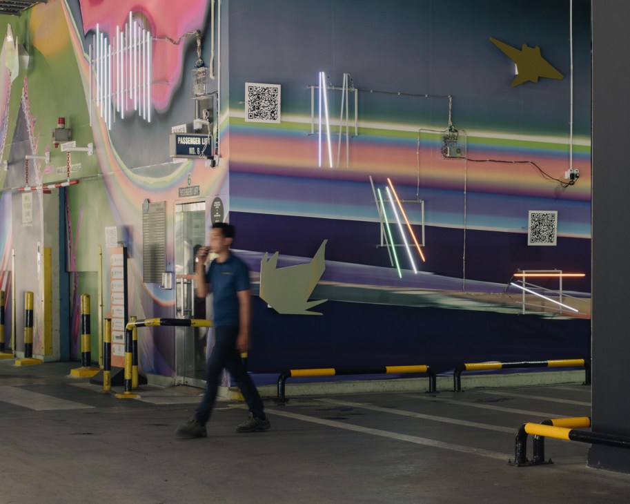 Colorful mural with neon lights and geometric shapes in warehouse gallery space with person walking past.