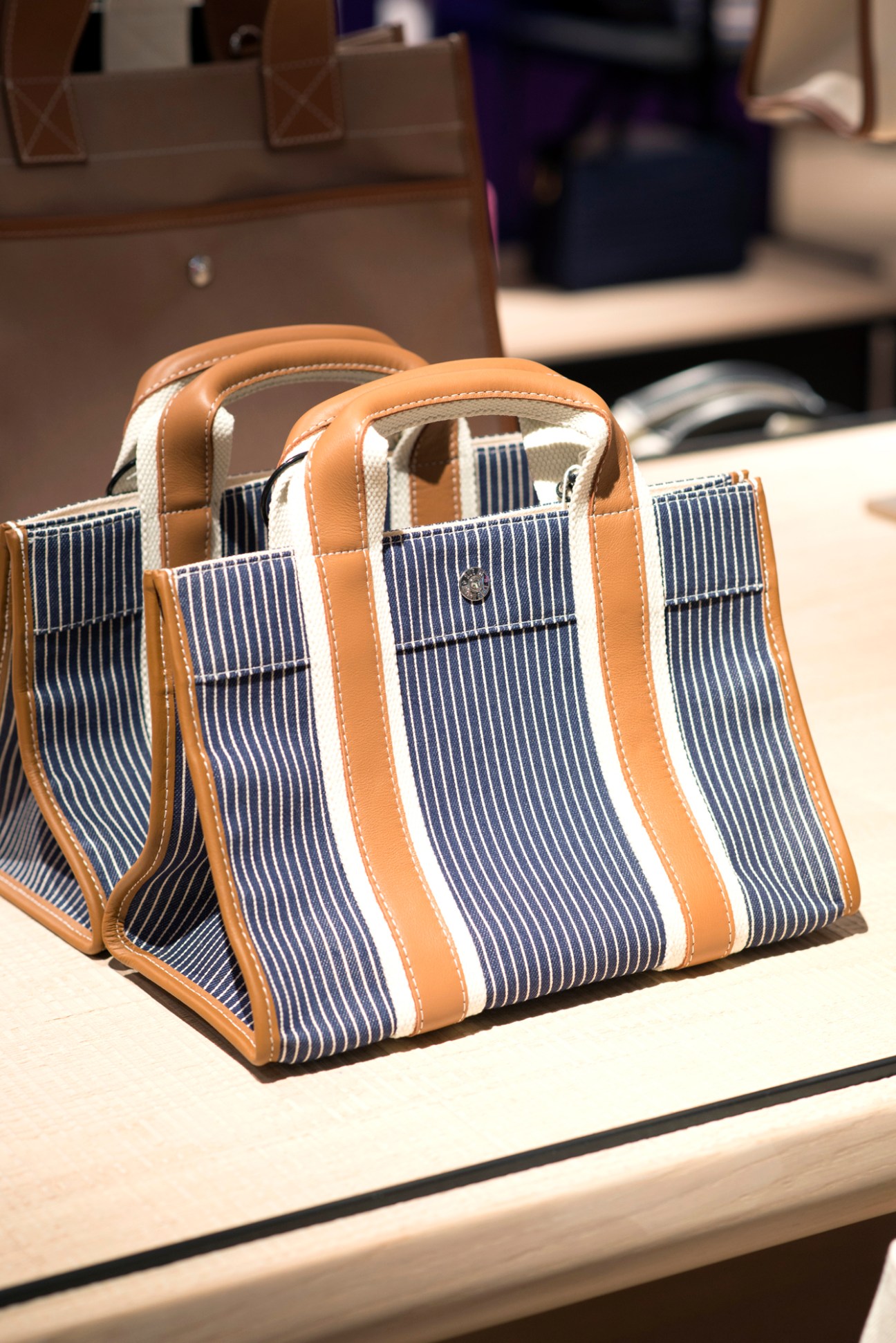 Blue and white striped handbag with tan leather handles and trim displayed on white surface