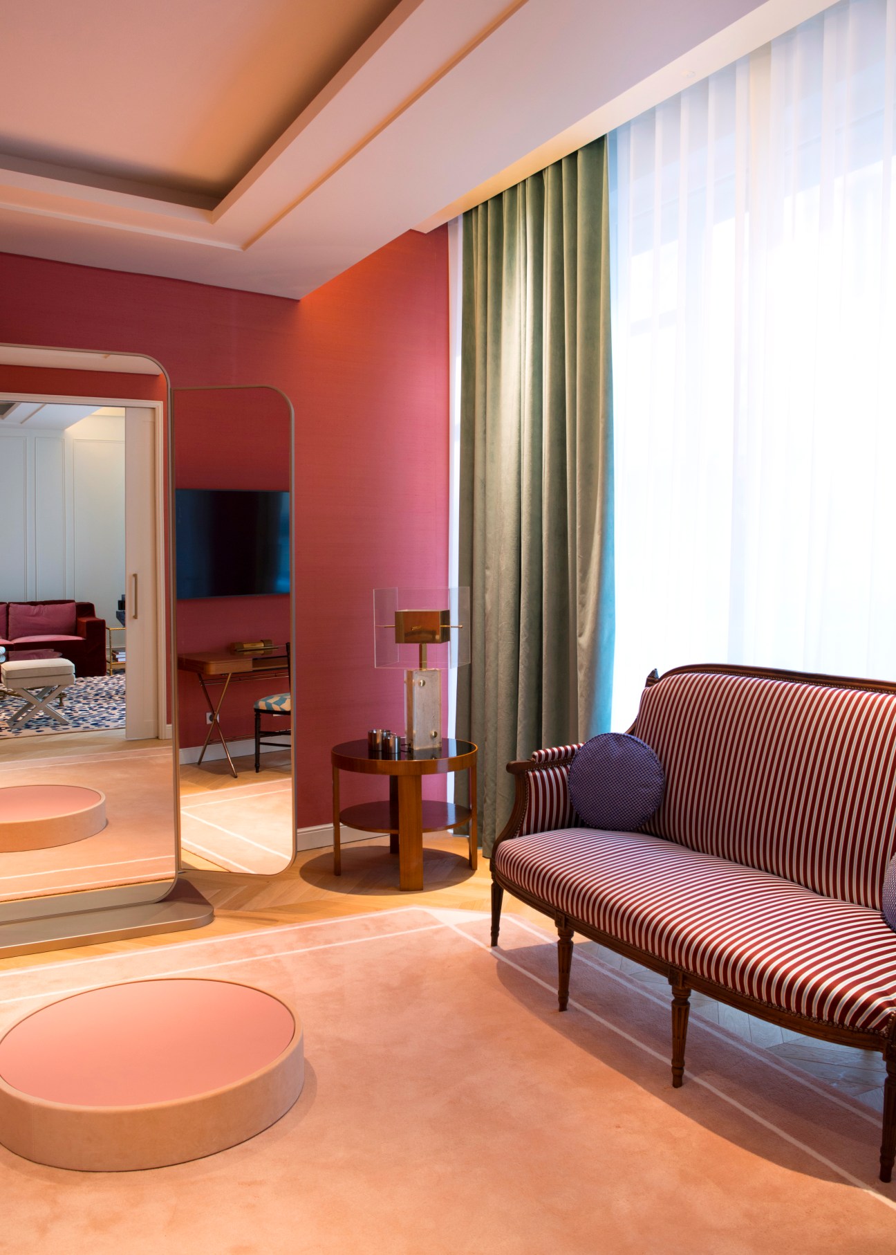 Modern hotel room interior with pink accent wall, striped upholstered chair, round mirrors and green curtains