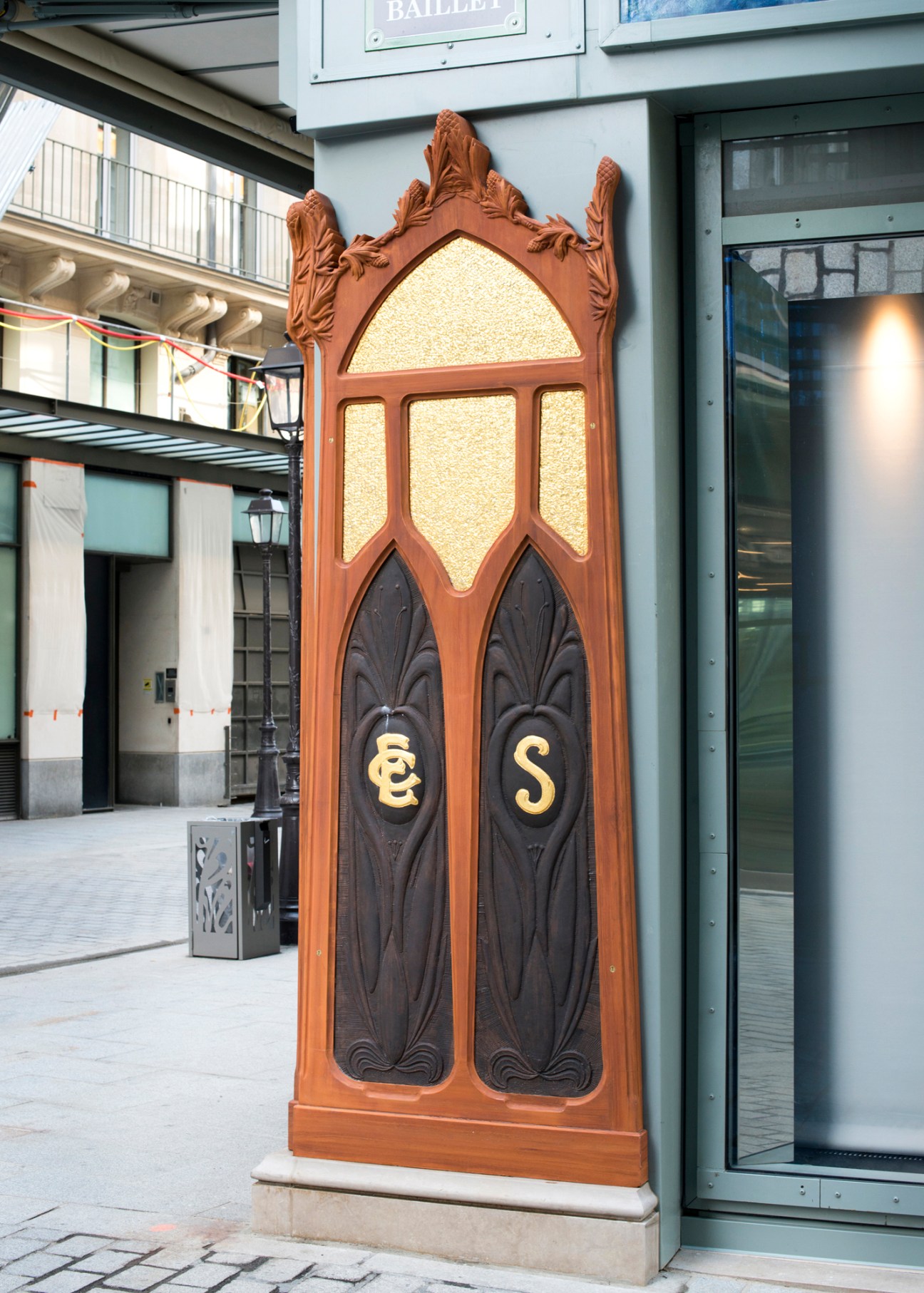 Ornate bronze relief sculpture with decorative carved elements and letters on building facade