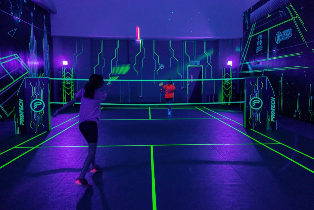 Players on a glow-in-the-dark badminton court with neon green lines and purple lighting at Shuttle in the Dark