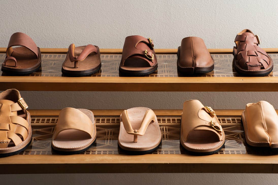 Collection of handcrafted leather sandals by Tokyo Sandal displaying various brown tones and designs on wooden shelves