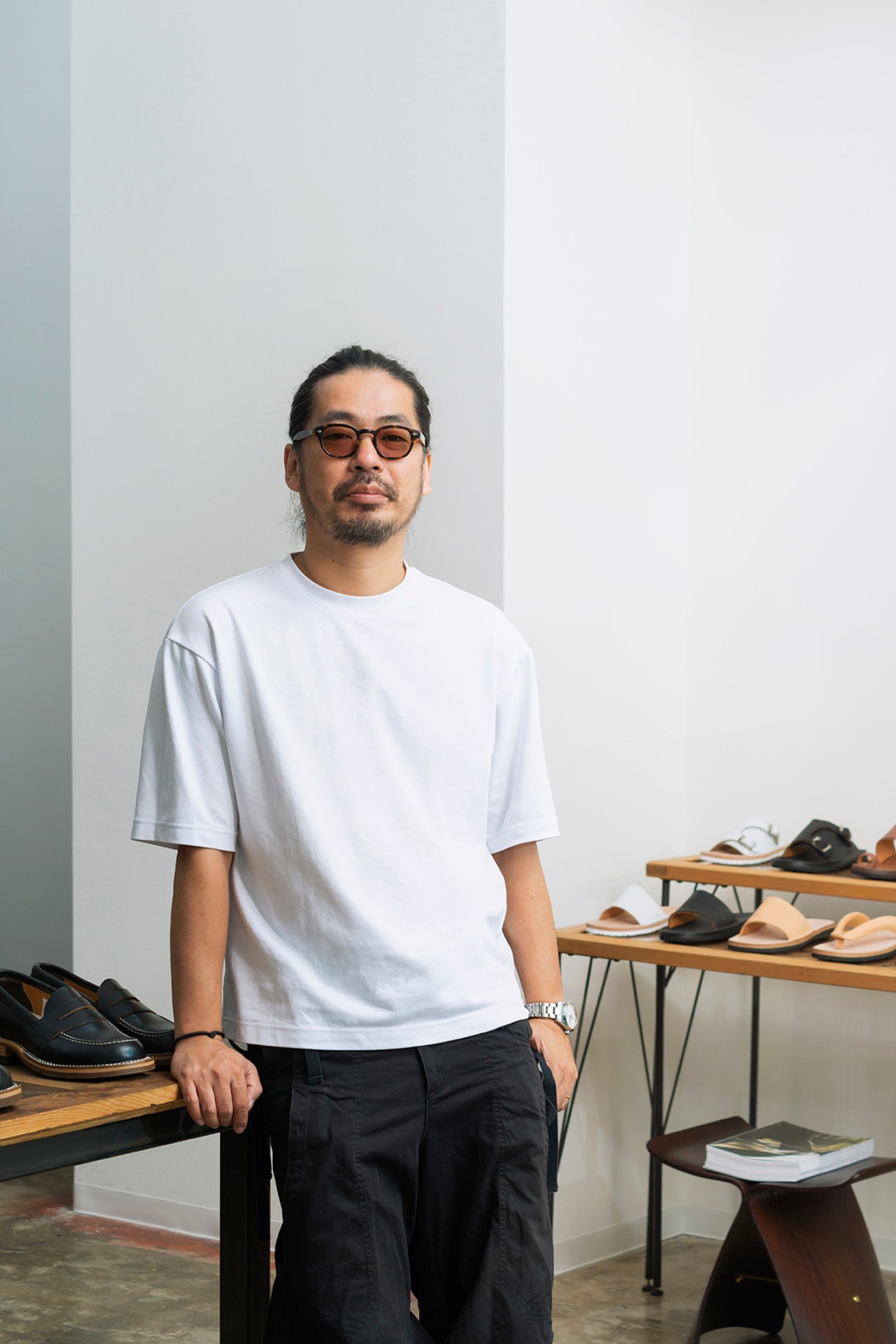 Katsuya Tokunaga standing in his Tokyo Sandal workshop surrounded by handmade leather sandals and shoemaking tools