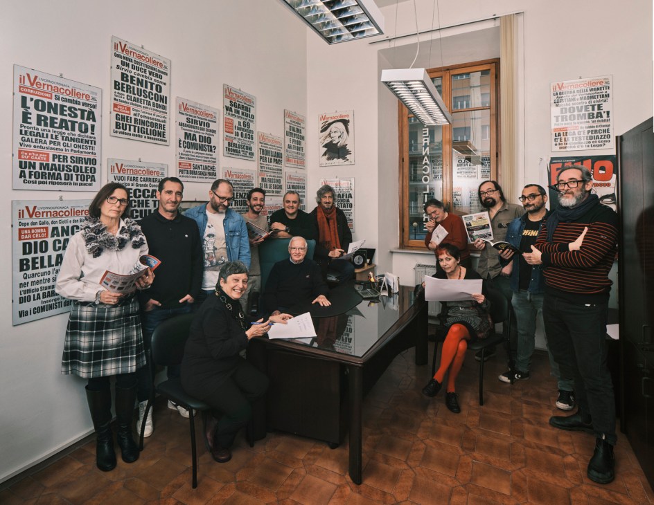 The editorial team of Il Vernacoliere newspaper gathered in their office surrounded by framed satirical newspaper front pages and posters