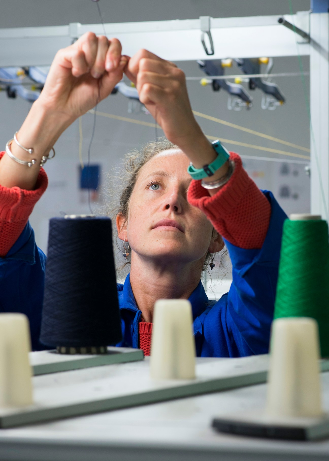 Worker examining textile thread with raised hands at Le Minor factory in Guidel, Brittany