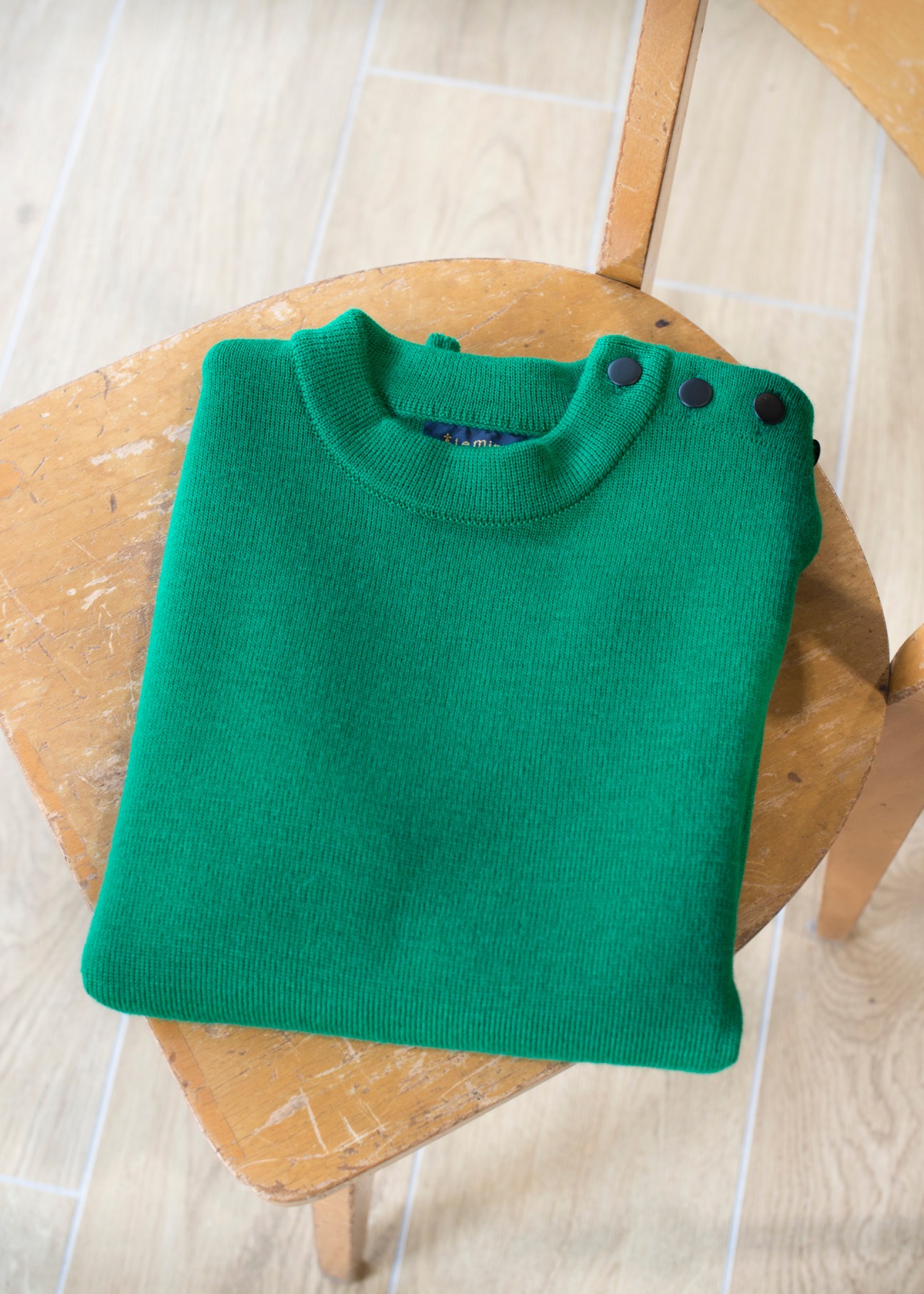Green knitted sailor jumper folded on wooden chair