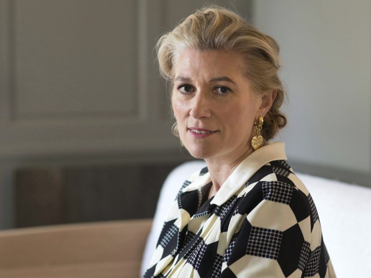 Marie-Claire Daveu sits at a wooden table wearing a geometric patterned black and white blouse
