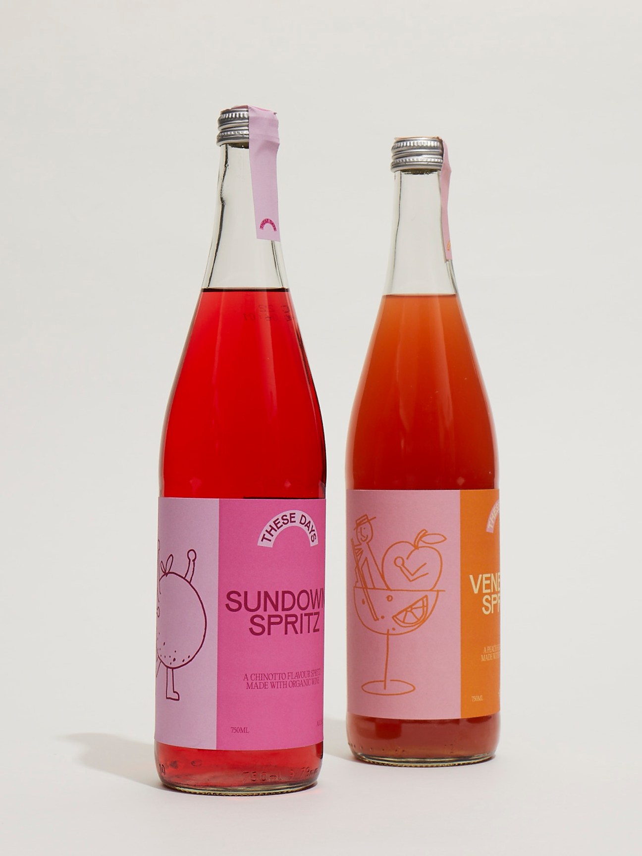Two bottles of These Days spritz - Sundown Spritz and Venetian Spritz - with pink and orange packaging and liquid