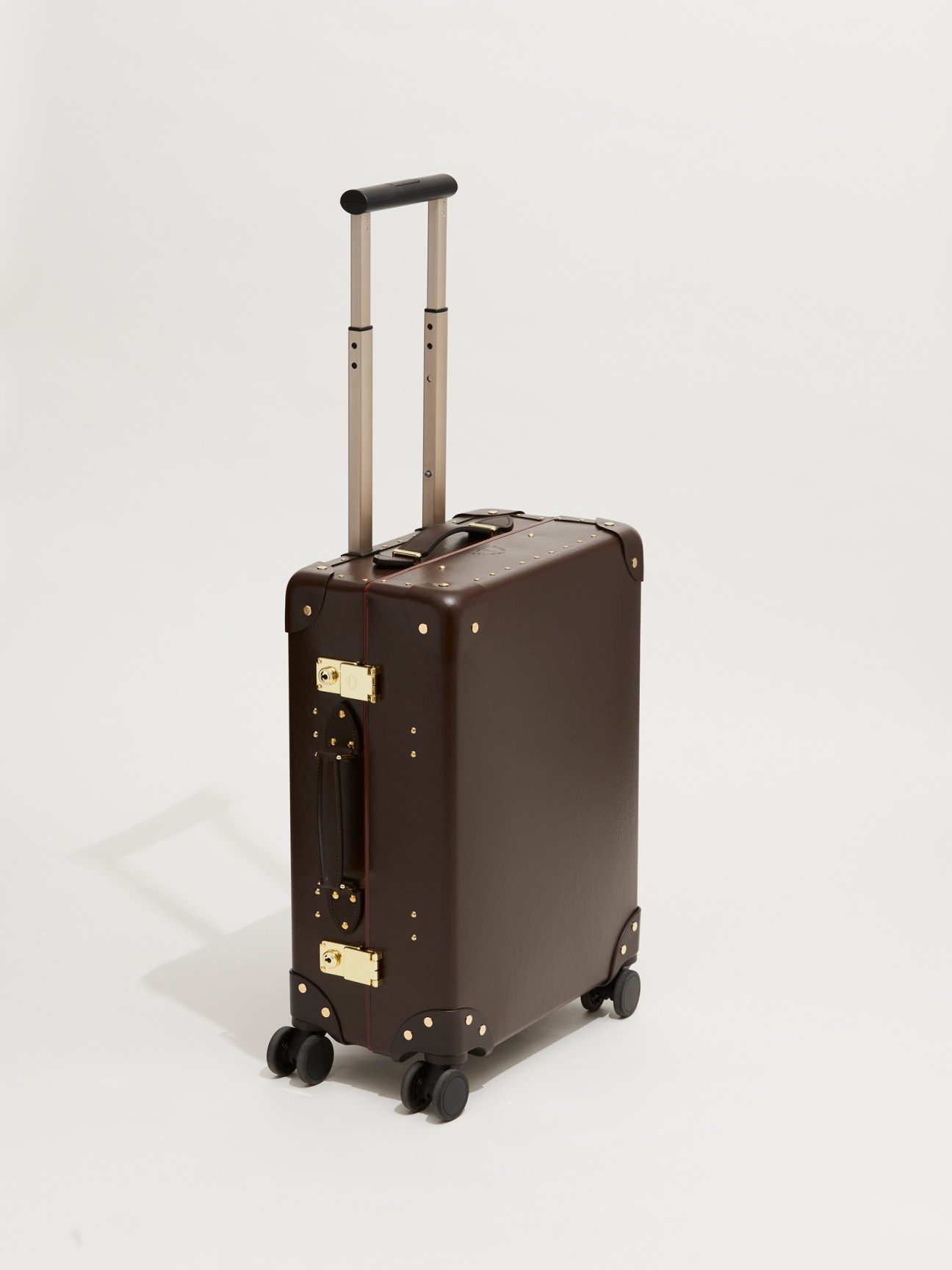 Brown leather suitcase with gold studs and brass hardware, featuring telescoping handle and wheels