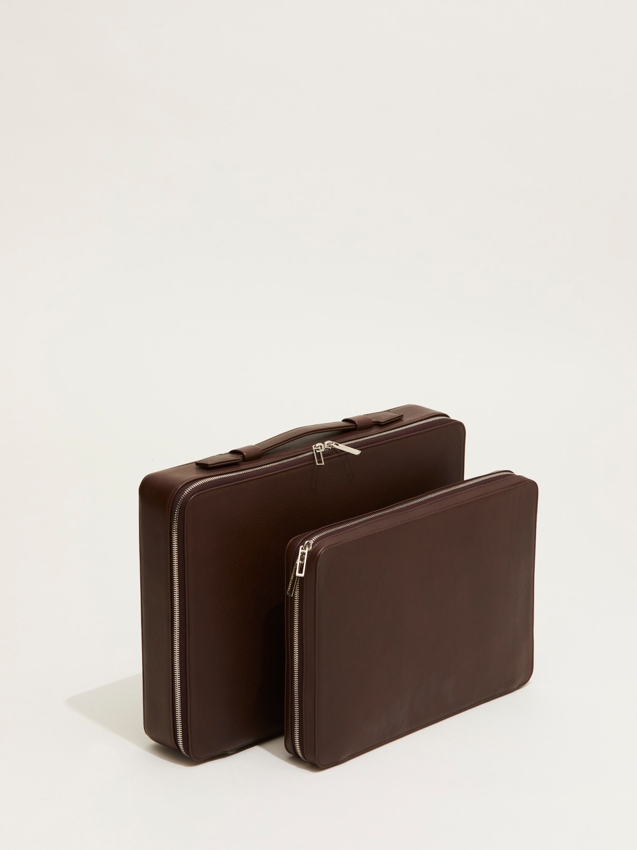 Two brown leather suitcases with zipper closures by Tsatsas x David Chipperfield on neutral background